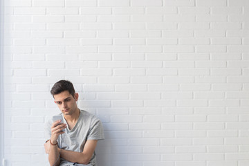 young man with mobile phone on white brick background