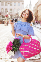 Happy smiling lady wearing trendy ruffled dress, straw hat, wrist watch, holding vintage camera,...