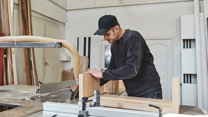 High Performance. High Quality. Carpenter cutting wood on electric saw at his workstation