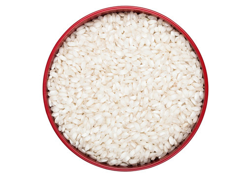 Red bowl of raw organic arborio risotto rice on white background. Healthy food.