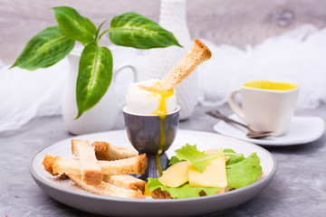 Soft boiled chicken egg, crackers, pieces of cheese and lettuce on a plate on the table. Ready to eat breakfast
