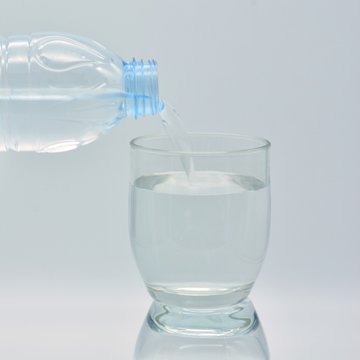 Botella de agua llenando un vaso de cristal