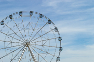 White Ferris wheel with glass light-blue cabins against the blue sky. Wheel in amusement park. Front view, copy space.