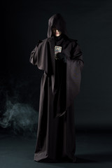full length view of woman in death costume holding tarot cards on black with smoke
