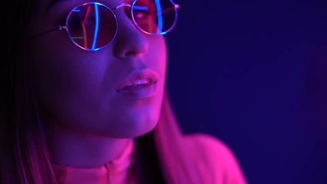 Fashionable girl in glasses on a neon background. Neon hearts are reflected in glasses.