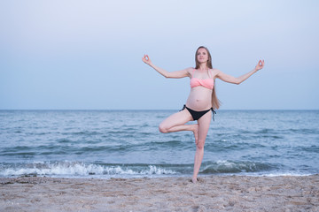 Fototapeta na wymiar Pregnant woman meditates on the beach. Yoga practice. Soft evening light