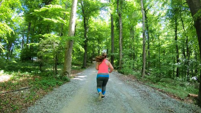 Right behind tracking shot of an overweight woman running up the hill in the forest