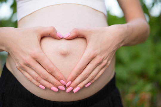 Female hands in a heart shape on her belly. Pregnant concept. Close-up