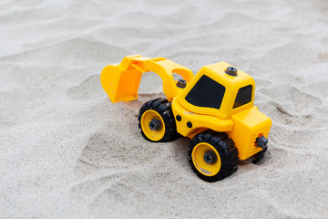 Yellow excavator toy in the sand, on the beach. toys for boys
