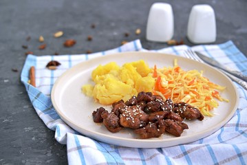 Sticky Indian style spiced chicken with a side dish of boiled potatoes and fresh cabbage salad on a white clay plate. Indian food.