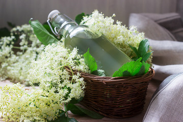 Homemade syrup of elderberry flowers in a glass jar and elder branches on a wooden table Rustic style.