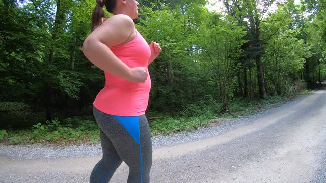 Tracking shot of an overweight woman running on a gravel forest road