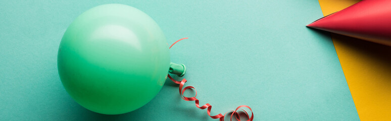 Panoramic shot of green balloon and red party hat on tiffany background
