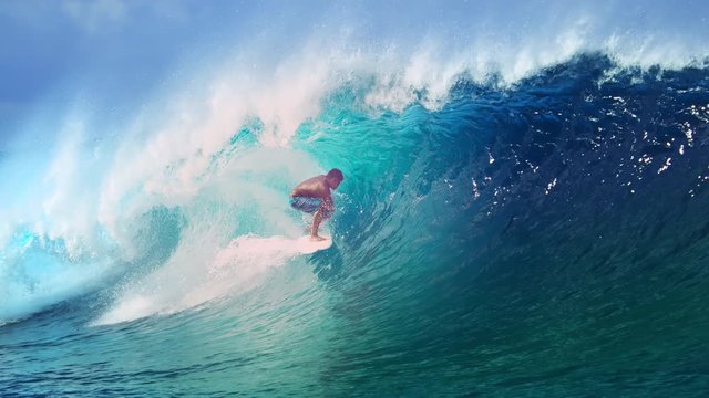 SLOW MOTION, CLOSE UP: Extreme athlete surfs a big barrel ocean wave glistening in the summer sunshine. Spectacular tube wave splashes over the surfer enjoying his active vacation in French Polynesia.