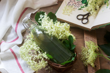 Homemade syrup of elderberry flowers in a glass jar and elder branches on a wooden table Rustic...