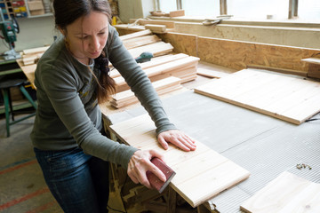 Young woman sanding wooden board using sand paper at workshop
