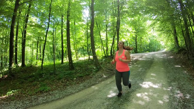 Tracking shot of a beautiful overweight woman running on a gravel road in the sunny forest