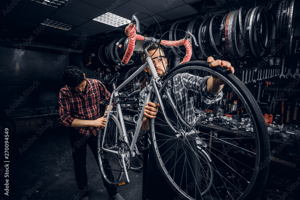 Wall mural Two attractive mans are working on bicycle fixing at busy workshop.