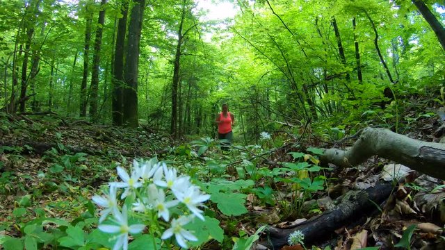 Locked down shot of a woman running up a path through a green and lush forest