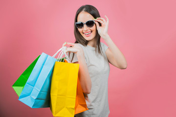 Fototapeta na wymiar Portrait of an excited beautiful girl wearing sunglasses holding shopping bags 