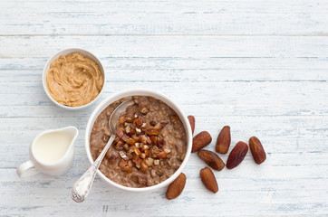 Delicious oatmeal in a white bowl, dates fruits, cocoa and vegan milk