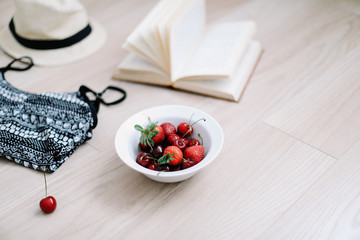 Top view travel or vacation concept. Swimsuit, hat, book and fresh sweet cherries and strawberries on wooden background.  Flatlay. Summer background. 