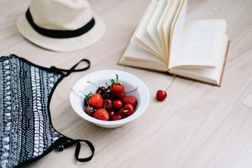 Top view travel or vacation concept. Swimsuit, hat, book and fresh sweet cherries and strawberries on wooden background.  Flatlay. Summer background. 
