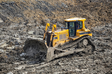 Obraz premium Yellow dozer pushes large piles of dirt