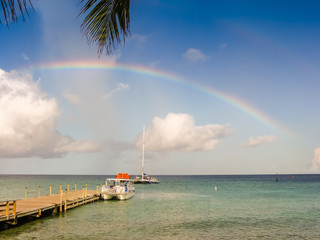 Rainbow above smooth ocean with boats tied to wooden pier - double rainbow - ideallic summer holiday with palm framing top of shot