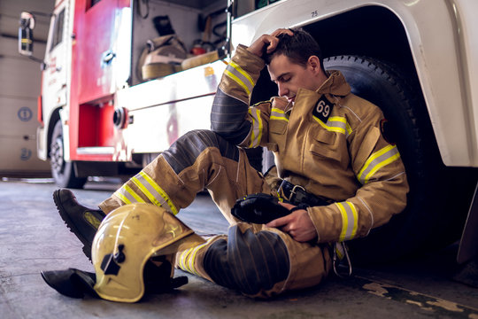 Photo of tired fireman sitting on floor near fire truck