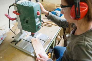 Young woman with drill perforating wood plank at workshop