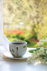 A cup of tea on a sunny table in a flowered garden, selective focus. Flowering trees in the background in the garden with a natural bokeh effect