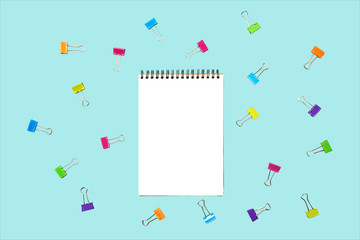 Back to school background with notepad, colorful paper clips on pastel blue backdrop. Flat lay, top view, copy space.