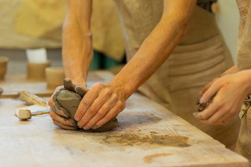 Strong man tightly pressing piece of fresh clay on a wooden table