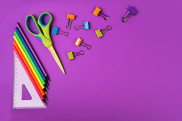 Back to school background with pencils, square ruler, scissors, colorful paper clips on purple backdrop. Flat lay, top view, copy space.