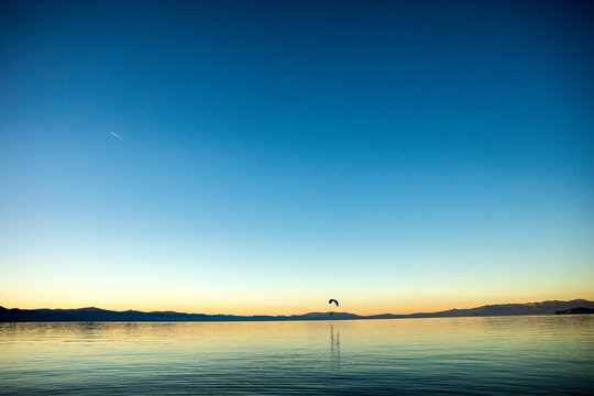 A landscape of Lake Tahoe at sunset with a para glider flying over it.