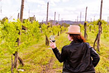 Girl in a hat with a glass of red wine in her hands and a bottle. Girl in the vineyards at sunset. Italian province and hills. Selective focus.