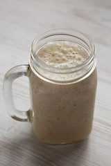 Banana smoothie in a glass jar over white wooden background, side view. Close-up.