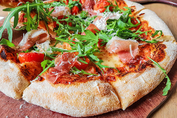Closeup of a traditional italian pizza with: ham,  mushrooms, cherry tomatoes, mozzarella, arugula on a wooden board ( high details).