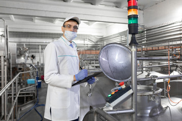 Inspector in a mask and a scrub stands with a folder-tablet in his hands at the dairy plant