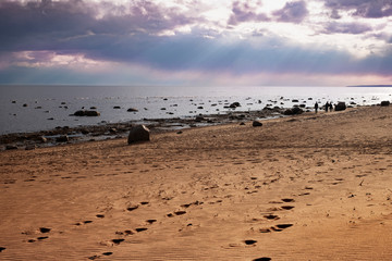 Footprints in the sand going to the sea. Sunset, the sun's rays breaking through the leaden clouds.