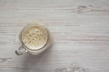 Banana smoothie in a glass jar over white wooden surface, top view. Flat lay, overhead, from above. Copy space.