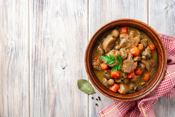 Turkey meat stew with mushrooms and vegetables in ceramic bowl on wooden table. Top view. Copy space.