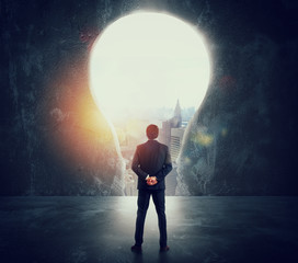 Fototapeta premium Businessman looks at a big hole on the wall shaped as a light bulb