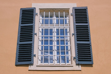 window in a German old house on a building painted in apricot color with green window shutters, whith cloud reflections