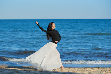 Fototapeta na wymiar Classical dancer woman. Charming ballerina with windy hair in white chiffon skirt dancing by the sea background. Sun shines on her. Horizontal. 