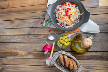 The concept of Russian national cuisine as a trend in the food 2019. Sauerkraut in a black ceramic dish on an old wooden table with ingredients laid out around. Vegetables with olive oil
