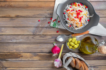 The concept of Russian national cuisine as a trend in the food 2019. Sauerkraut in a black ceramic dish on an old wooden table with ingredients laid out around. Vegetables with olive oil