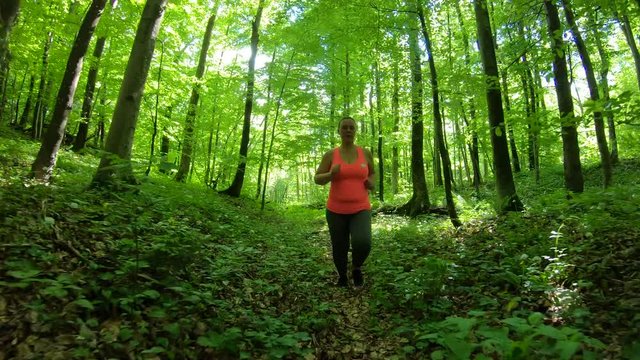 Tracking shot of an overweight woman running in the forest with sun peeking through the trees
