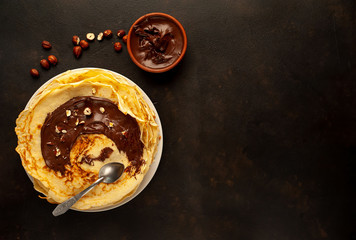 Pancakes with chocolate paste and hazelnuts, on a white plate on a background of concrete, slate with copy space for your text